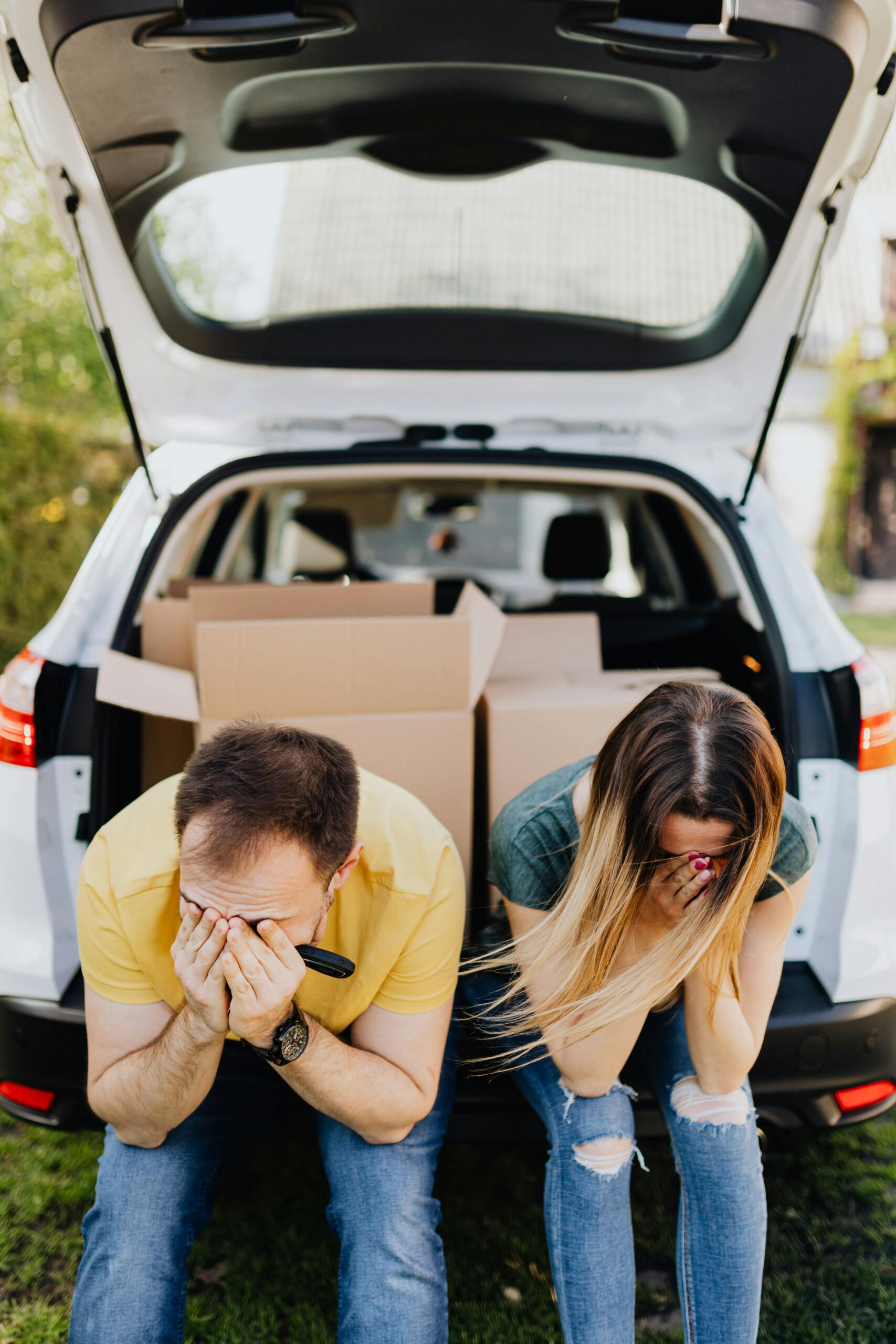 A distressed couple sits by a car full of boxes, symbolizing moving stress.